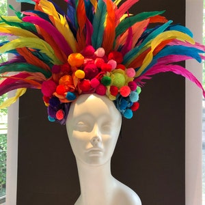 May include: A colorful headpiece with a rainbow of feathers and pom-poms. The headpiece is made of bright colors, including red, orange, yellow, green, blue, and purple.