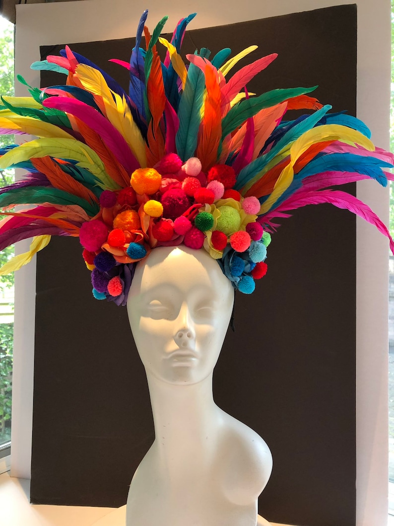 May include: A colorful headpiece with a rainbow of feathers and pom-poms. The headpiece is made of bright colors, including red, orange, yellow, green, blue, and purple.