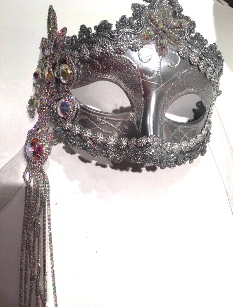 May include: A silver masquerade mask with a beaded fringe and iridescent rhinestones. The mask has a delicate, ornate design and is perfect for a costume party or special occasion.