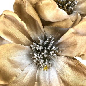 K&ouml;nnte beinhalten: Nahaufnahme von zwei gro&szlig;en, k&uuml;nstlichen Blumen mit geschichteten, goldbraunen Bl&uuml;tenbl&auml;ttern. Die Zentren weisen eine Ansammlung von silberfarbenen, strukturierten Akzenten auf. Die Blumen dienen wahrscheinlich dekorativen Zwecken, m&ouml;glicherweise f&uuml;r die Heimdekoration oder zum Basteln.
