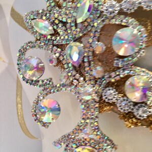 May include: A close-up of a decorative piece featuring a gold and silver design with iridescent rhinestones. The rhinestones are arranged in a floral pattern.