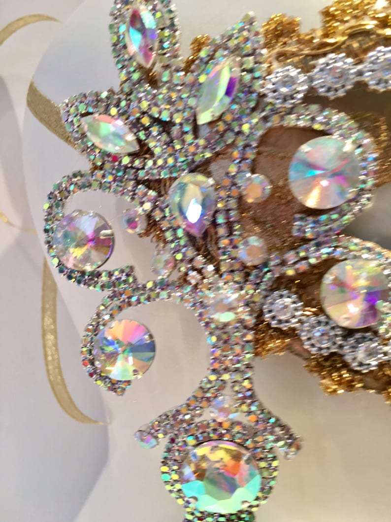 May include: A close-up of a decorative piece featuring a gold and silver design with iridescent rhinestones. The rhinestones are arranged in a floral pattern.
