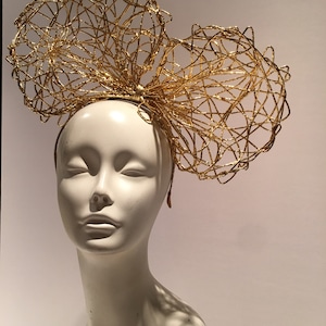 May include: A gold wire headband with a large bow on top. The bow is made of multiple layers of wire that are intertwined to create a delicate and intricate design.