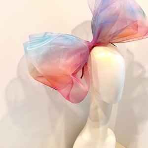 Könnte beinhalten: Ein großer, bunter, Ombre-Schleife aus durchsichtigem Stoff. Die Schleife ist zu einem großen Knoten gebunden und wird auf einem weißen Mannequin-Kopf präsentiert.