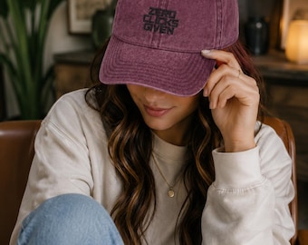 May include: A maroon baseball cap with a distressed, washed-out finish. The front of the cap features the text "ZERO CLICKS GIVEN" embroidered in black thread. The cap has a curved brim and a structured crown with ventilation eyelets on top.