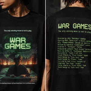 May include: A black t-shirt featuring a War Games movie poster graphic on the front with a person at a computer and the text The only winning move is not to play. The back displays the title War Games and a list of credits in green text.