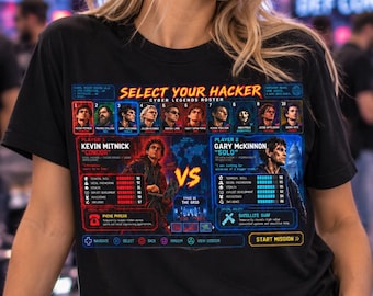 May include: A black t-shirt featuring a Select Your Hacker graphic print. The design displays a cyber legends roster, player stats for Kevin Mitnick and Gary McKinnon, a versus icon, and game controller button prompts at the bottom.