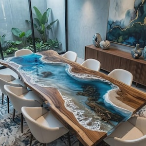 Könnte beinhalten: Ein großer rechteckiger Esstisch mit einer Massivholzplatte mit Naturkante und einer zentralen Harzeinlage, die eine tropische Küstenlinie mit blauem Wasser, weißem Schaum und Sanddetails darstellt, umgeben von sechs weißen Stühlen.