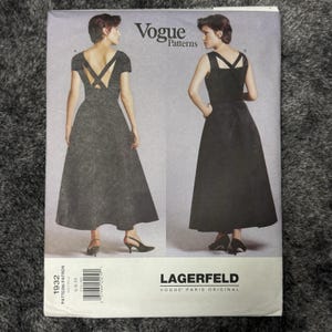Könnte beinhalten: Ein Vogue Patterns Schnittmusterumschlag für ein Kleid, beschriftet mit 1932 Lagerfeld Vogue Paris Original. Die Vorderseite zeigt zwei Ansichten eines dunklen, bodenlangen Kleides mit einem taillierten Oberteil, einem weiten Rock und Trägern.