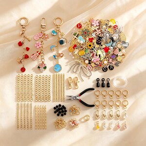 Può includere: Un kit per la creazione di gioielli con tre portachiavi dorati assemblati, un vasto assortimento di ciondoli in smalto colorato, catene in metallo dorato, anellini, chiusure a moschettone, perline nere e una pinza in metallo con manici neri.