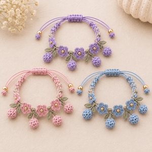 May include: Three adjustable bracelets featuring crocheted floral and berry motifs in lavender, pink, and light blue. Each bracelet includes green crocheted leaves, small gold-toned beads at the center of the flowers, and gold-toned end beads.
