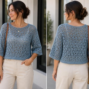 May include: A dusty blue crochet top featuring a wide boat neckline, three-quarter length sleeves, and a loose, open-knit pattern. The garment is cropped at the waist and is worn over a white camisole, paired with light beige trousers and a straw bag.