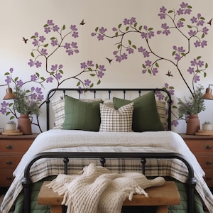 May include: A black metal bed frame with a white and gray plaid duvet cover and a white knitted throw blanket. The headboard is decorated with a floral wall decal featuring purple flowers and brown branches.