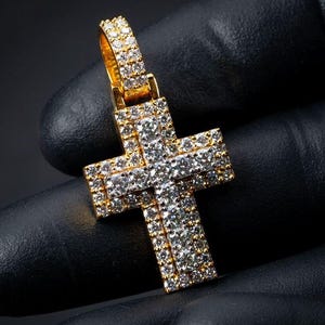 May include: A gold-toned cross pendant featuring a multi-layered design completely encrusted with numerous small, clear, round-cut stones. The pendant includes a matching gold-toned bail at the top, also set with stones, creating a uniform, sparkling appearance.