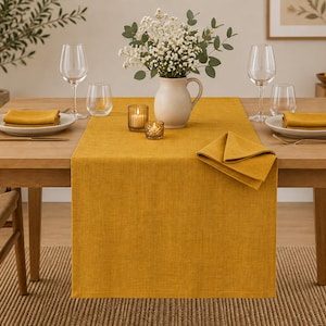 Può includere: Un runner da tavola rettangolare color giallo senape su un tavolo da pranzo in legno chiaro. La tavola è apparecchiata con due piatti bianchi, ciascuno con un tovagliolo piegato color senape, due calici da vino, due bicchieri e due portacandele.