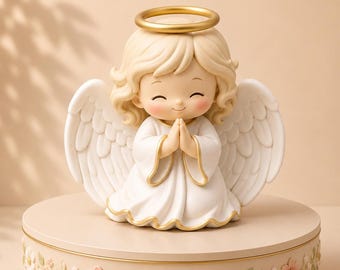 Può includere: Una piccola statuetta di angelo con capelli biondi, un'aureola dorata e ali bianche, che indossa una veste bianca con bordi dorati. L'angelo ha le mani giunte in preghiera e poggia su un piedistallo rotondo beige decorato con rilievi floreali.