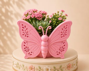 Può includere: Un vaso a forma di farfalla rosa chiaro con intricati intagli floreali sulle ali e un corpo segmentato. Il vaso contiene una pianta succulenta verde e piccoli fiori rosa, poggiato su una base rotonda color crema con un motivo a tralci.