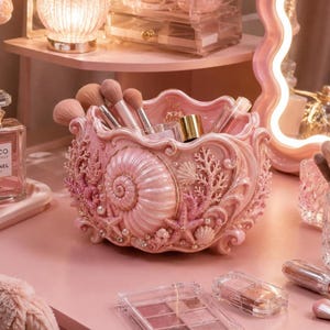 May include: A light pink decorative bowl featuring a sculpted seashell, coral, and starfish design. The bowl is filled with various makeup brushes and cosmetic items, showcasing a textured, pearlescent finish with small embedded pearl accents.