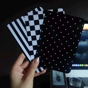 Può includere: Tre carte rettangolari con angoli arrotondati caratterizzate da distinti motivi in bianco e nero. Una carta presenta strisce verticali, la seconda un motivo a scacchi e la terza è nera con un design a pois bianchi.