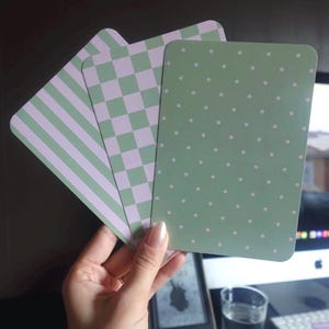 Peut inclure: Trois cartes rectangulaires aux coins arrondis présentant des motifs distincts dans des tons de vert sauge et de lavande douce. Une carte affiche des rayures verticales, la deuxième un motif à damier et la troisième des pois blancs.