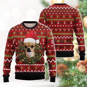 Op de afbeelding: Een rode trui met lange mouwen en ronde hals met een herhalend patroon van groene en witte geometrische vormen, kerstbomen en hondensilhouetten. De voorkant toont een chihuahua met een kerstmuts in het midden van een kerstkrans.