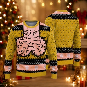 May include: A long-sleeved crewneck jumper in mustard yellow and light pink. The front features a large, central pink graphic resembling a brain. The design includes black and white geometric patterns, horizontal bands, and white snowflake motifs.