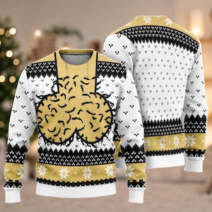 May include: A long-sleeve crewneck jumper featuring a white, black, and gold colour scheme. The front displays a large, central graphic of two rounded, textured shapes in gold. The garment is patterned with black and white geometric motifs and snowflakes.