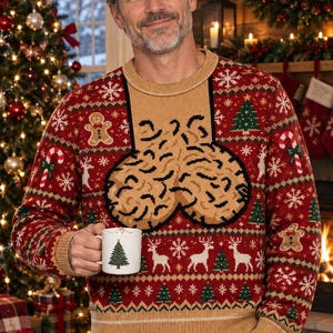 May include: A red and tan knit jumper featuring a graphic of two textured tan shapes on the chest, surrounded by patterns of gingerbread men, candy canes, reindeer, and Christmas trees. A white mug with a green tree graphic is held in one hand.