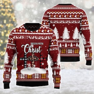 May include: A red long-sleeve jumper featuring a black crew neck and cuffs. The front displays the text "Christmas BEGINS WITH Christ" above a cross with plaid and leopard patterns, a snowman, and white pine trees with a snowflake pattern.