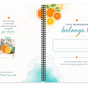 May include: A spiral-bound workbook with white pages featuring orange fruit illustrations, teal watercolor accents, and small orange hearts. The text reads: This workbook belongs to, A plan is more than a list, and Every small step you take today.
