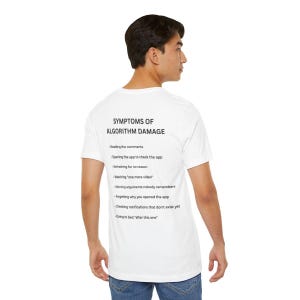May include: A white t-shirt featuring black text on the back that reads SYMPTOMS OF ALGORITHM DAMAGE followed by a list of behaviors including reading comments, refreshing for no reason, watching one more video, and checking notifications.