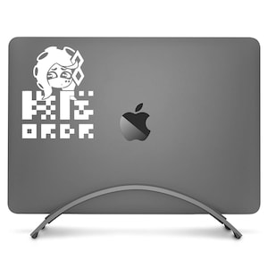 May include: A gray laptop with a white graphic of a character and pixelated text. The text reads "Kiki Order". The laptop is on a silver stand, and the Apple logo is visible.