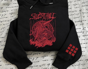 May include: A black hooded sweatshirt featuring a red graphic print on the chest with the text Silent Hill and a pyramid-headed figure. The left sleeve displays a red grid of nine squares. The hoodie includes a drawstring hood and ribbed cuffs.