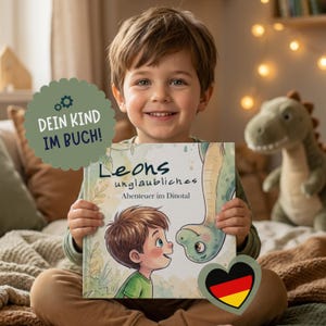 Könnte beinhalten: Ein Kinderbuch mit festem Einband, betitelt Leons unglaubliches Abenteuer im Dinotal, mit einer Illustration eines Jungen und eines grünen Dinosauriers auf dem Cover sowie einem salbeigrünen runden Aufkleber mit dem Text DEIN KIND IM BUCH.