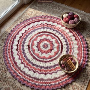 May include: A round crochet blanket featuring a circular mandala design in shades of cream, pink, and purple. The blanket has a scalloped edge and is displayed with a bowl of yarn balls and a bowl of wooden crochet hooks. Text reads Round About Crochet Blanket Pattern and Instant pdf download.