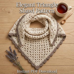 May include: A cream-colored crocheted triangle shawl with a scalloped brown border. The text Elegant Triangle Shawl Pattern and Instant PDF Download is visible. A mug of tea and a wooden spoon are nearby, along with a sprig of dried lavender.