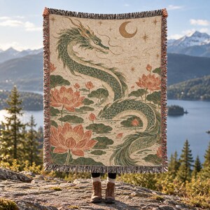 May include: A woven throw blanket featuring a large green dragon winding through a pond filled with orange lotus flowers and lily pads. The background is a light beige color with a crescent moon and small stars depicted in the upper right corner.