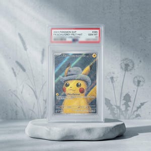 Puede incluir: Una carta coleccionable Pokemon SVP 2023 Pikachu with Grey Felt Hat, calificada como GEM MT 10, encapsulada en una funda protectora de plástico transparente. La carta muestra un Pikachu amarillo con un sombrero gris sobre un fondo texturizado.