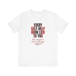 May include: A white short-sleeved t-shirt featuring red text that reads: EVERY SELF-HELP BOOK LIED TO YOU, followed by the smaller, italicised red text: the answer was always deeper. The shirt has a crew neckline and a standard fit.