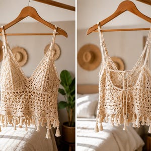 May include: A beige crochet camisole top featuring a V-neckline, adjustable spaghetti straps, and an intricate openwork pattern. The hem is finished with a row of dangling tassels. The back includes two sets of tie closures for an adjustable fit.
