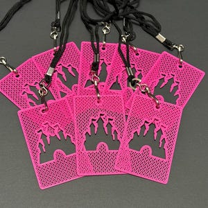 May include: A collection of six rectangular, bright pink plastic badge holders, each featuring a die-cut silhouette of a castle. Every badge holder is attached to a black fabric lanyard by a silver-toned metal swivel hook and a split ring.