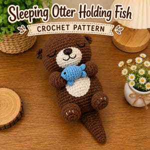 Può includere: Un giocattolo a forma di lontra addormentata lavorato all'uncinetto in marrone che tiene un piccolo pesce lavorato all'uncinetto blu. La lontra ha pancia e muso color crema con gli occhi chiusi. Il testo "Sleeping Otter Holding Fish CROCHET PATTERN" è sopra.