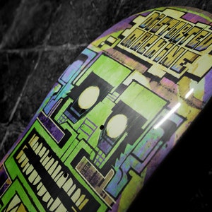May include: A green, purple, and yellow skateboard deck with the words "Defeated Machine" printed on it.