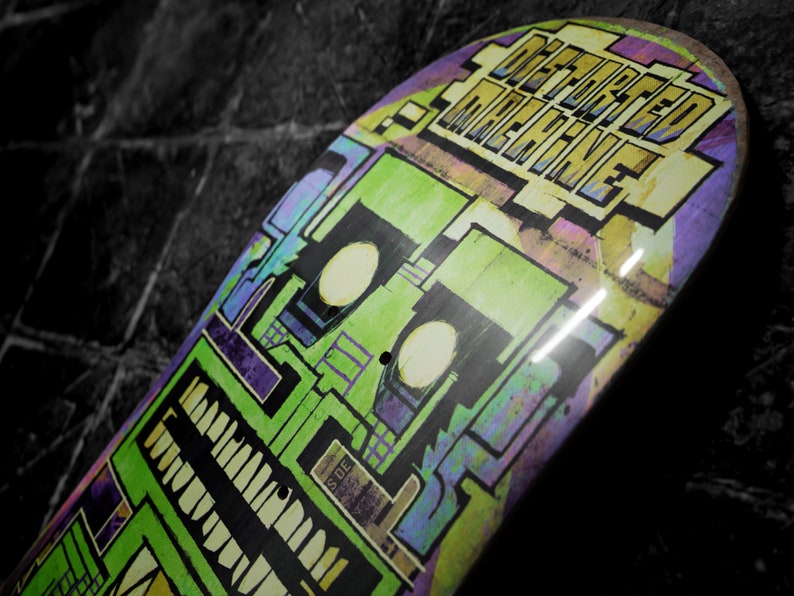 May include: A green, purple, and yellow skateboard deck with the words "Defeated Machine" printed on it.