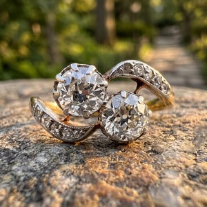 May include: A bypass ring crafted from yellow gold featuring two prominent round-cut clear stones set in prongs. The split shank design curves around the center stones and is accented with a series of smaller round-cut clear stones along the band.