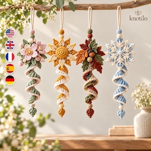 Könnte beinhalten: Vier hängende Häkelornamente mit dem Text knotilo. Jedes zeigt ein einzigartiges Motiv: rosa Blüten, eine gelbe Sonnenblume, Herbstblätter mit Eichel und eine blaue Schneeflocke. Darunter befindet sich jeweils ein spiralförmiger Häkelschwanz.