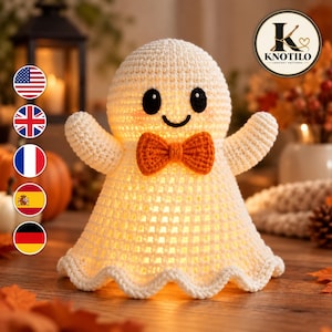 May include: A cream-coloured crocheted ghost figure featuring a bright orange bow tie, black embroidered eyes, and a curved black mouth. The hollow body is illuminated from within, casting a warm glow through the textured yarn stitches.