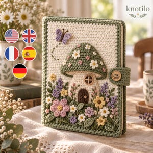 May include: A rectangular crochet book cover featuring a central mushroom house motif with a green cap and brown door. The design includes colourful flowers, green leaves, and a small purple butterfly. A green tab with a wooden button secures the cover.