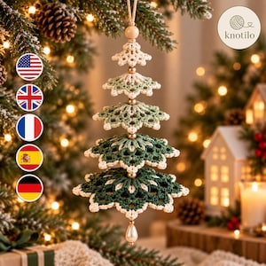 May include: A hanging Christmas tree ornament crafted from crocheted yarn in shades of cream, sage green, and dark forest green. The tiered design features five layers separated by small gold-toned beads, with a cream-coloured bead at the top.