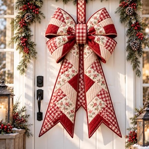 May include: A large, quilted fabric bow decoration featuring a patchwork design of red and white gingham, striped, and floral patterns. The bow has two long, pointed tails hanging down and is centred on a white door with a black handle.